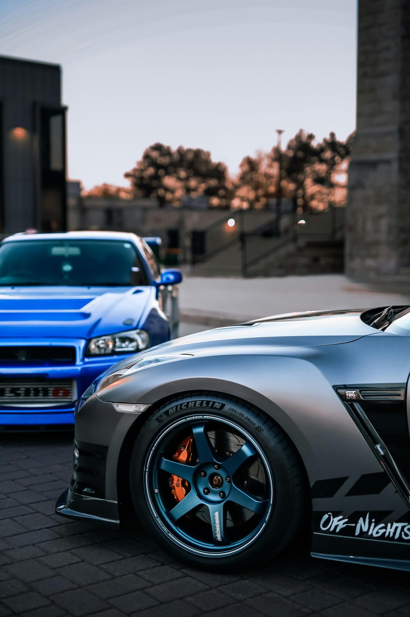 Close-up view of two sports cars parked in an urban area at sunset.